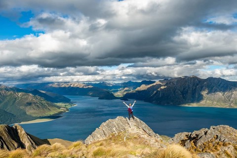 Hiker stands on a rock and stretches her arms in the air