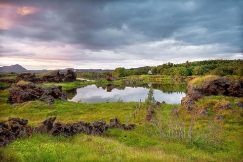 Lava formations of volcanic rock rise from green meadows with dramatic skies at Kalfastroend