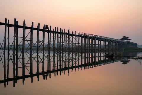 Buddhist monks walk across the U-leg bridge in red robes as the sun rises