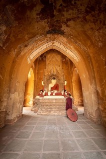 Buddhist young monk in red robe with red umbrella standing in a temple and praying