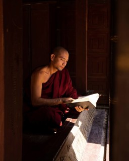 Buddhist monk in red robe reading ancient scriptures in a pagoda