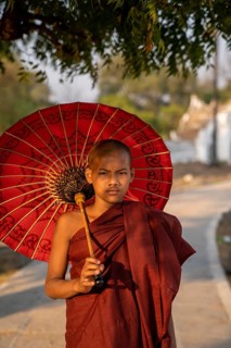 Buddhist monk stands with red umbrella on a path
