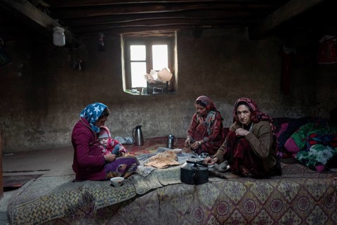 A woman with an infant and two other woman sitting on carpets in the living room of a traditional mud house