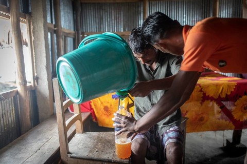 Honey collectors fill nectar from a bucket into plastic bottles