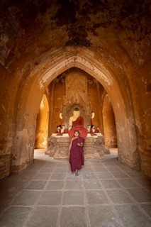 Buddhist young monk in red robe with red umbrella walks in a temple