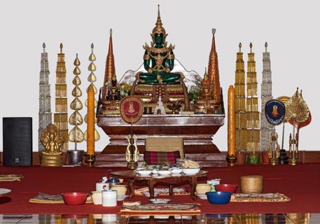 Donated food for monks in front of a small altar with a replica of the Emerald Buddha in meditation pose