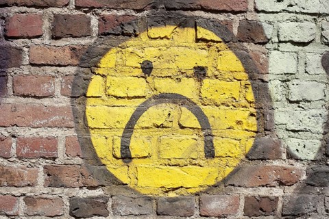 Yellow sad smiley painted on a brick wall