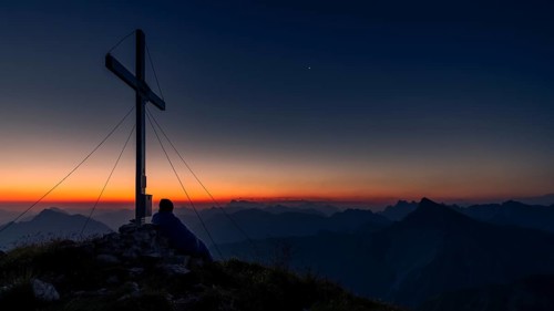 Cross of the Kreuzspitze at sunrise with mountaineer at the summit