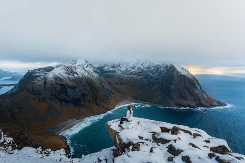 Woman sitting on a viewing platform on a mountain in front of Kvalvika beach