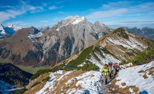 Three hikers on a hiking trail with snow in autumn