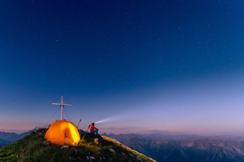 Cross of the Kreuzspitze by a starry sky with tent and mountaineer at the summit