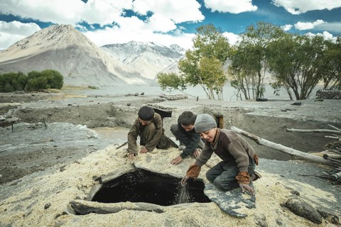 Three boys shovel wheat grains through the opening from above into a granary