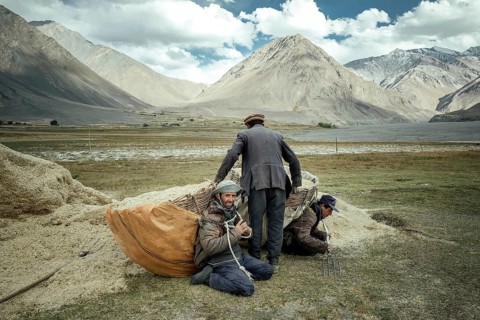 One man helps two other men shoulder their baskets of wheat to bring the harvest from the fields to the granaries