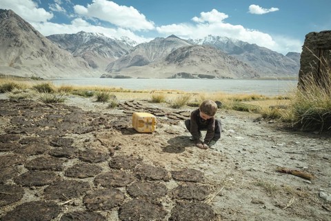 Boy plays next to cow dung flat cakes