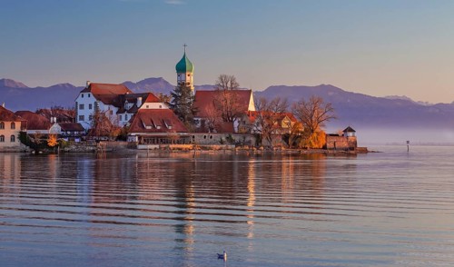Peninsula with the parish church of St. George in front of the Alps in the evening sun