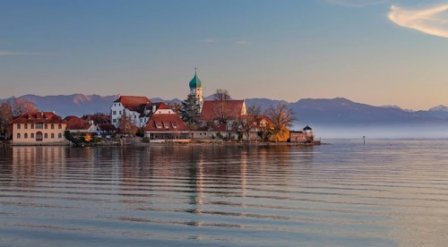 Peninsula with the parish church of St. George in front of the Alps in the evening sun