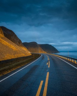 Road leading to rainbow with dramatic sky and sunset light