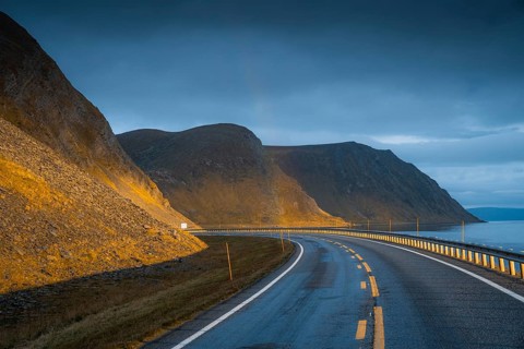 Road leading to rainbow with dramatic sky and sunset light