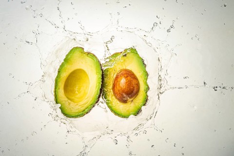 Two halves of avocado splashing into clear water