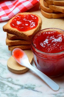 Strawberry jam in glass with spoon and rusk