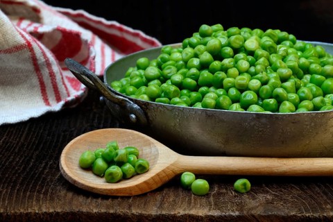 Defrosted green peas in shell with cooking spoon