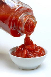 Tomato ketchup flows from bottle into bowl