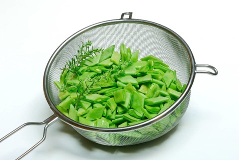 Sliced broad beans with savory in kitchen sieve