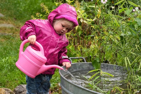 Little girl with rubber boots and rain jacket playing with water and watering can in the rain