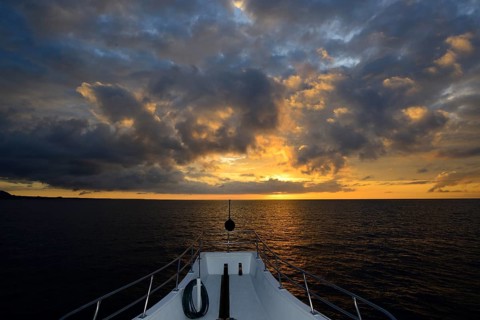 Bow of a ship in sunset with clouds over the Pacific Ocean