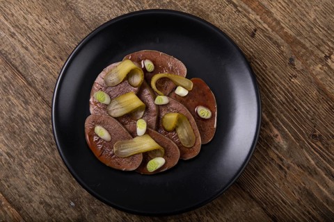Sliced beef tongue with cornichons on black plate
