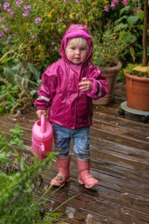 Little girl with rubber boots and rain jacket playing with water and watering can in the rain