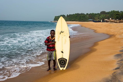 Local boy with his surfboard on a beach in Robertsport