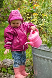 Little girl with rubber boots and rain jacket playing with water and watering can in the rain