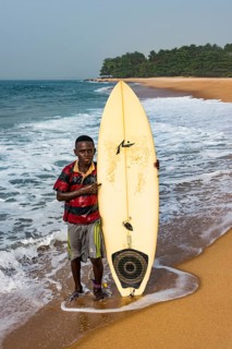Local boy with his surfboard on a beach in Robertsport
