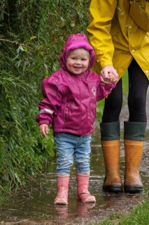 Little girl with rubber boots and rain jacket holding her mother's hand in the rain