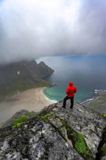 Hiker enjoys the view from Helvetestinden to the beach of Bunes