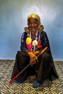 Chin Kaang hill-tribe woman with traditional facial tattoo and elaborate tribal earrings playing a flute with her nose