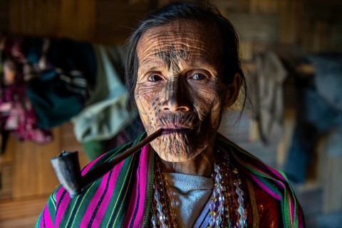 Chin woman with spiderweb tattoo smoking a pipe