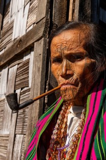 Chin woman with spiderweb tattoo smoking a pipe
