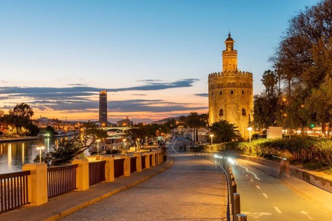 Boardwalk at the river Rio Guadalquivir with illuminated Torre del Oro
