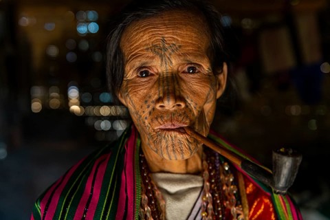 Chin woman with spiderweb tattoo smoking a pipe