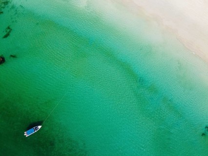Aerial of a little boat in the clear waters anchoring on a beach on Smart island
