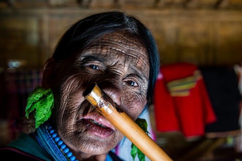 Chin woman with spiderweb tattoo blowing a flute with her nose