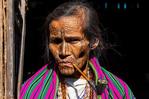 Chin woman with spiderweb tattoo smoking a pipe
