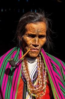 Chin woman with spiderweb tattoo smoking a pipe