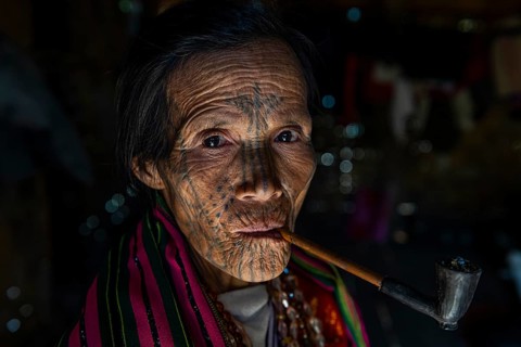 Chin woman with spiderweb tattoo smoking a pipe