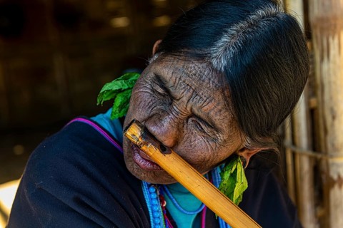 Chin woman with spiderweb tattoo blowing a flute with her nose