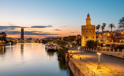 Boardwalk at the river Rio Guadalquivir with illuminated Torre del Oro
