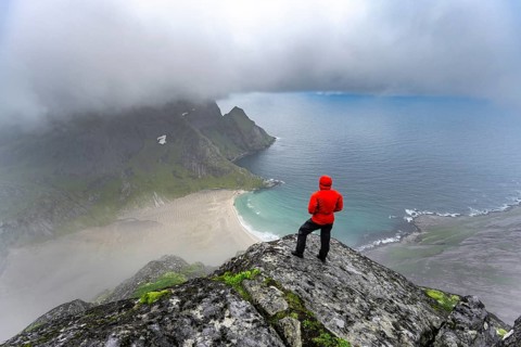 Hiker enjoys the view from Helvetestinden to the beach of Bunes