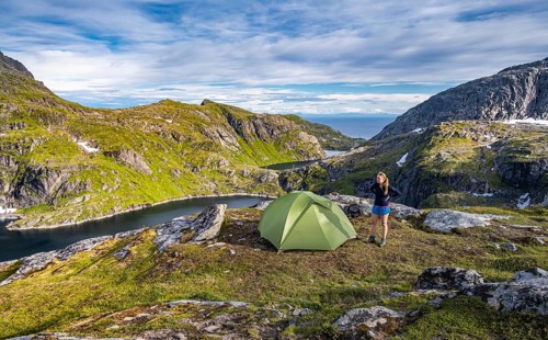 Hiker stands next to tent in the mountains